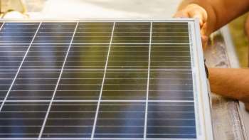 A person is handling a solar panel on a work surface.