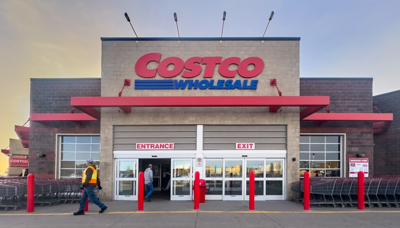 The exterior of a Costco Wholesale warehouse with shopping carts and a person walking by.