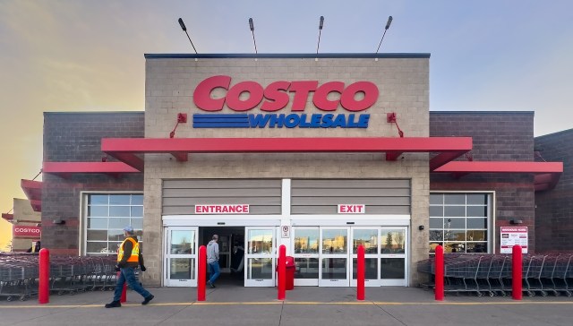 The exterior of a Costco Wholesale warehouse with shopping carts and a person walking by.