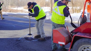 Two workers in neon vests repairing a pothole.