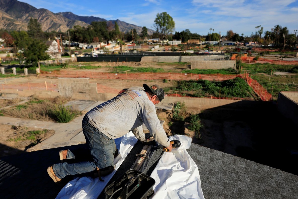 A man working on a roof with tools and a construction site visible in the background.