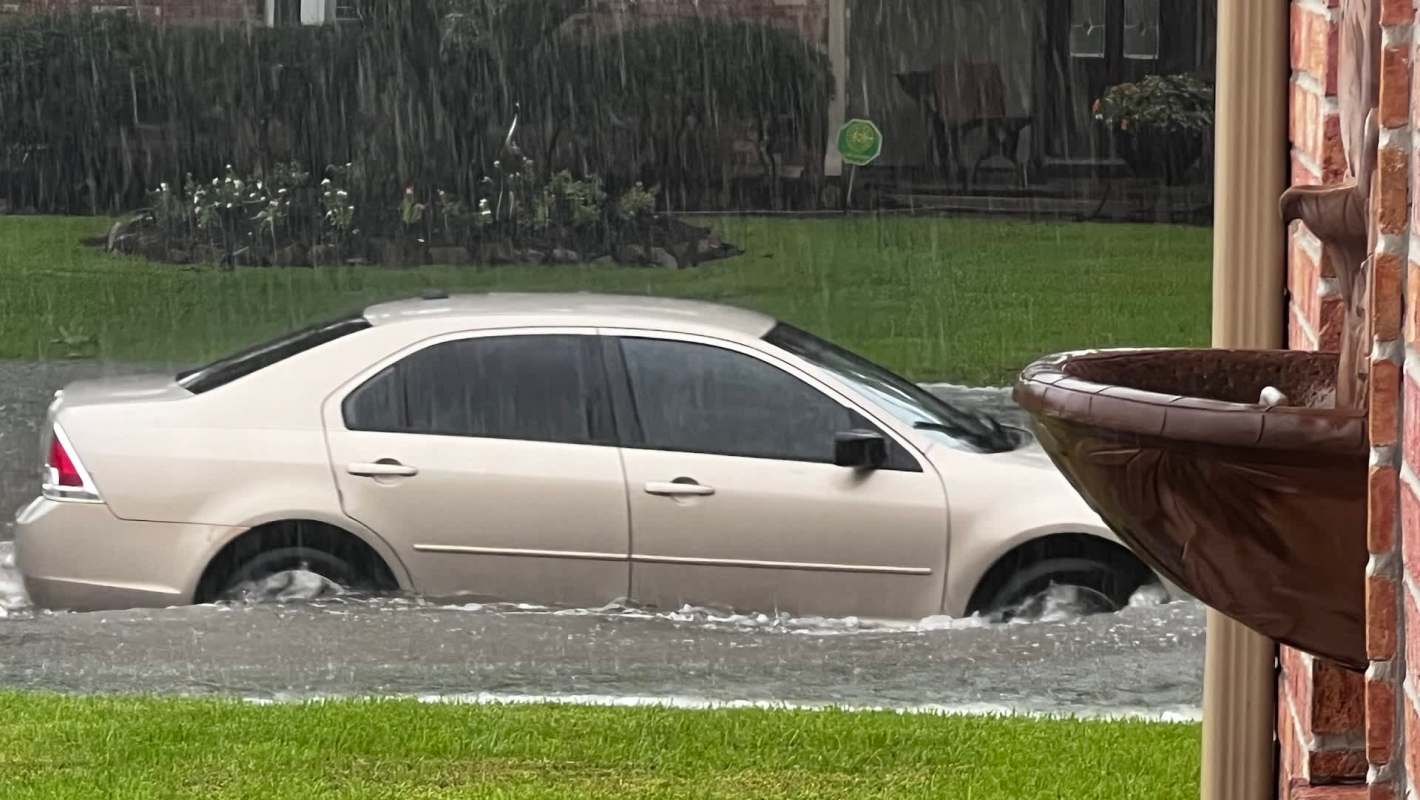 A car partially submerged in floodwater during heavy rain.