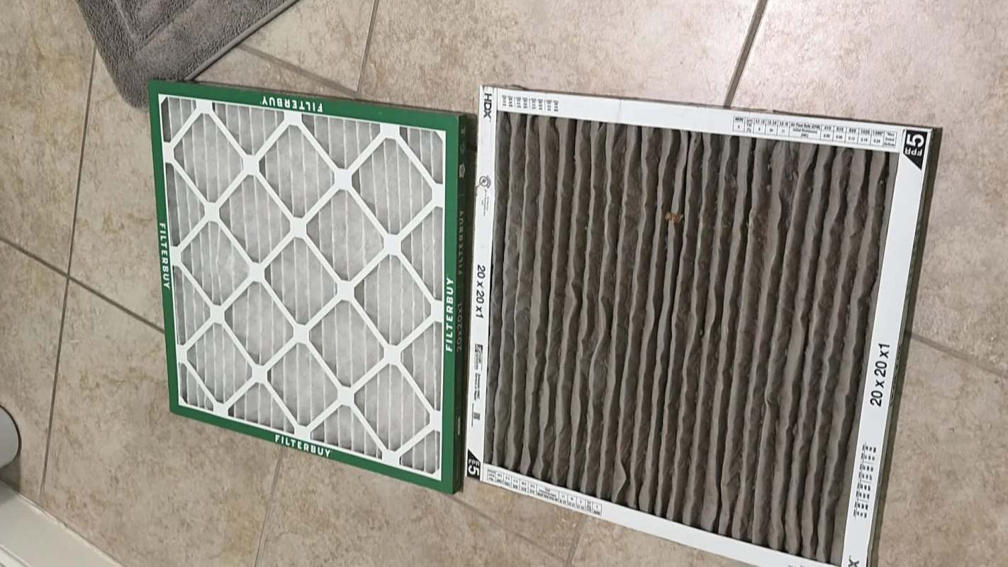 Two air filters, one clean and white and the other dirty and gray, placed on a tiled floor.
