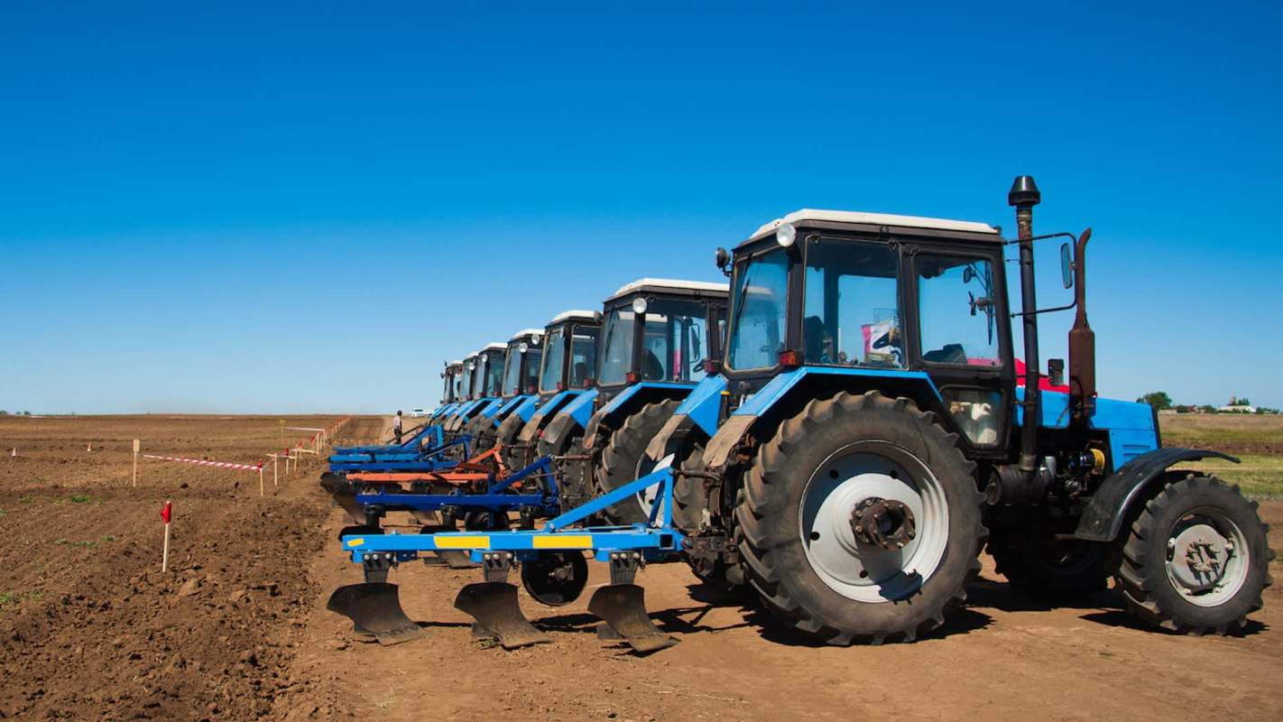 Several blue tractors lined up on a plowed field under a clear blue sky.
