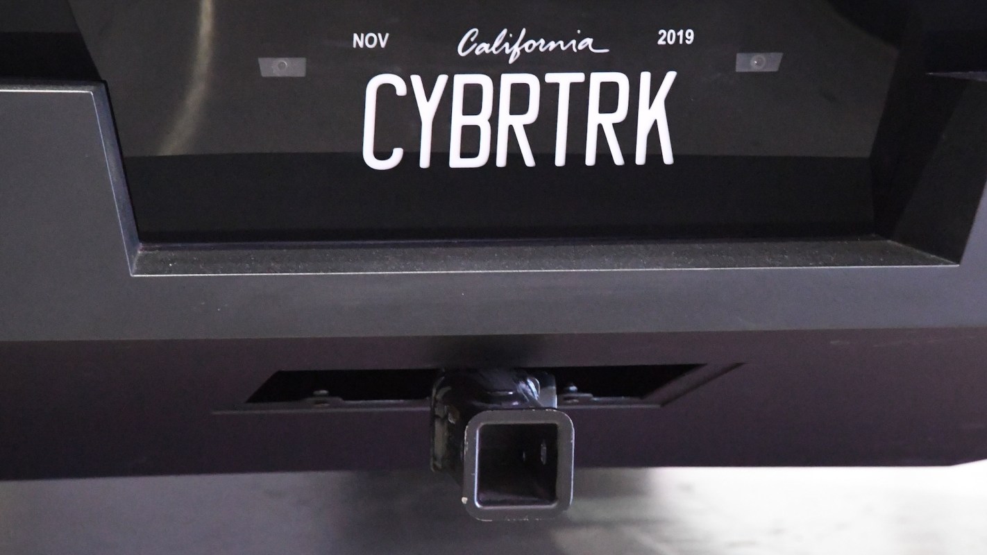 A black vehicle's rear with a custom license plate reading "CYBRTRK" and a tow hitch visible.