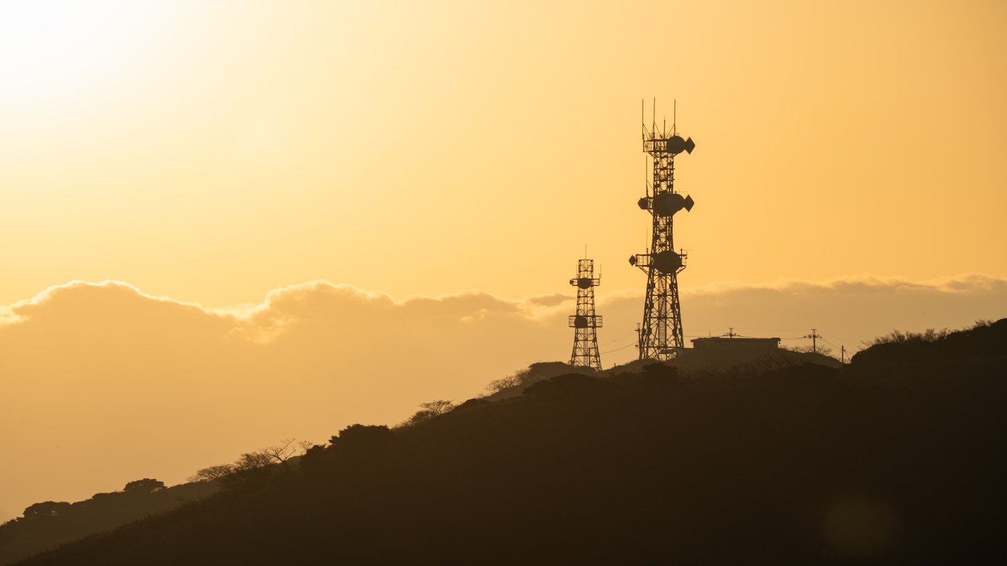 Communication towers silhouetted against an orange sunset.