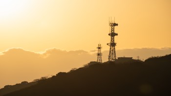 Communication towers silhouetted against an orange sunset.