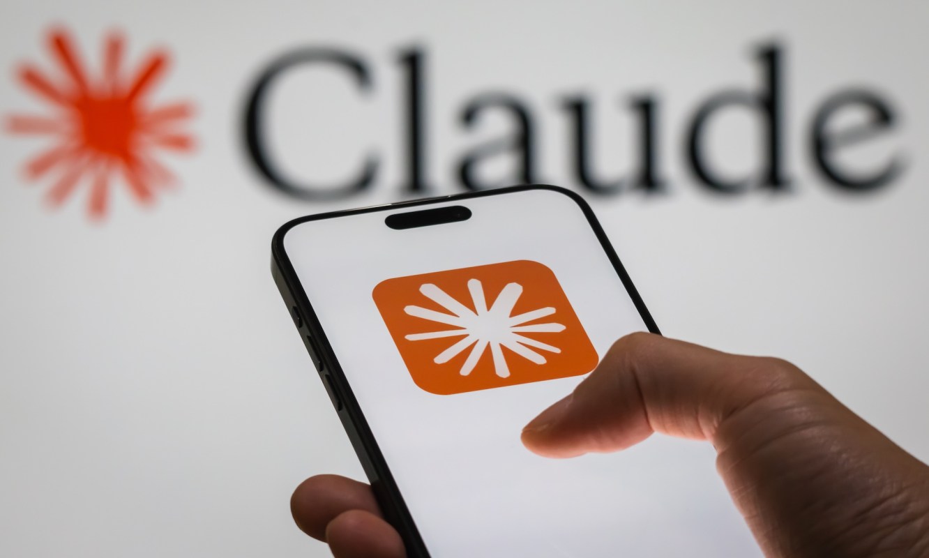 A hand holds a smartphone displaying an orange app icon, with "Claude" logo in the background.