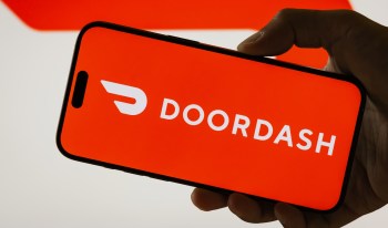 A hand holding a smartphone displaying the DoorDash logo on an orange background.