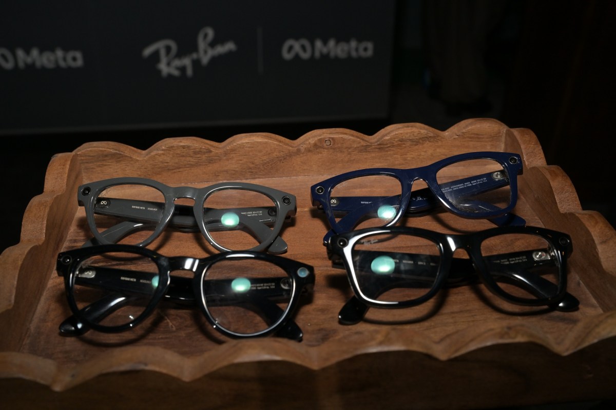Four pairs of glasses displayed on a wooden tray, with two black, one gray, and one blue frame.