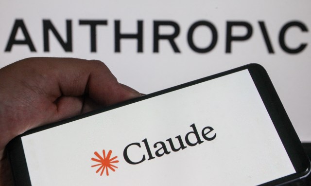 A hand holds a smartphone displaying the logo "Claude" in front of a background with the word "ANTHROPIC."