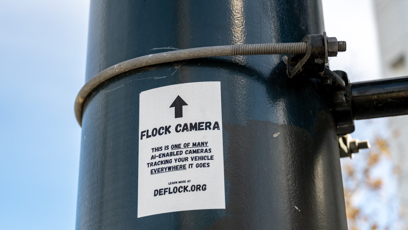 A sign on a pole indicating a Flock camera tracking vehicles.