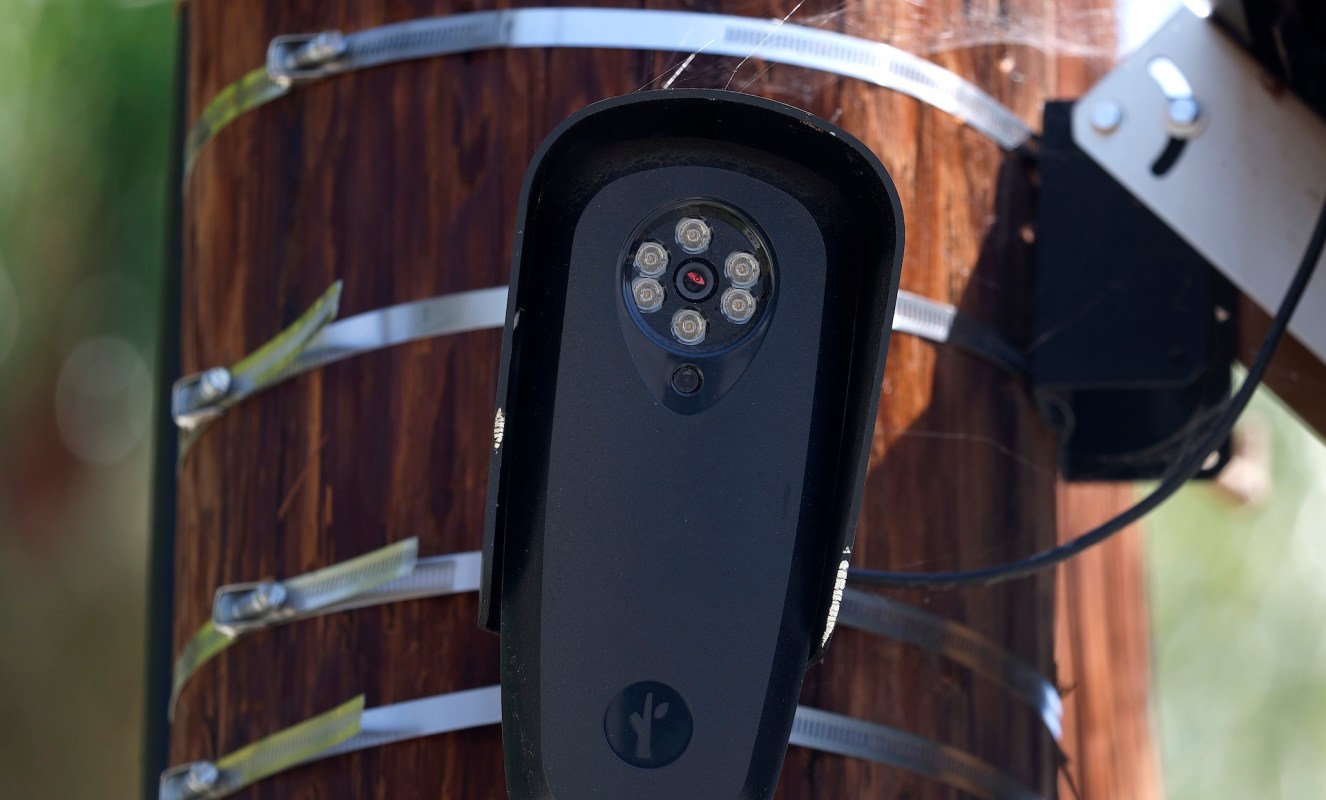 A Flock Safety surveillance camera mounted on a wooden utility pole with metal straps.