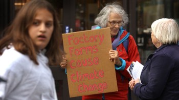 A woman holds a sign that reads "Factory Farms Cause Climate Change" while talking to another woman.