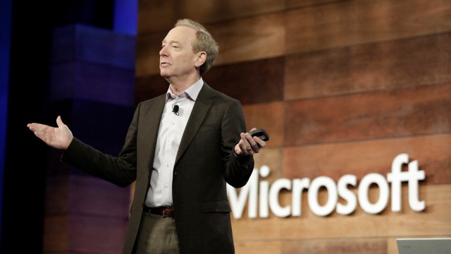 Microsoft President Brad Smith gesturing while presenting on stage in front of a Microsoft logo.