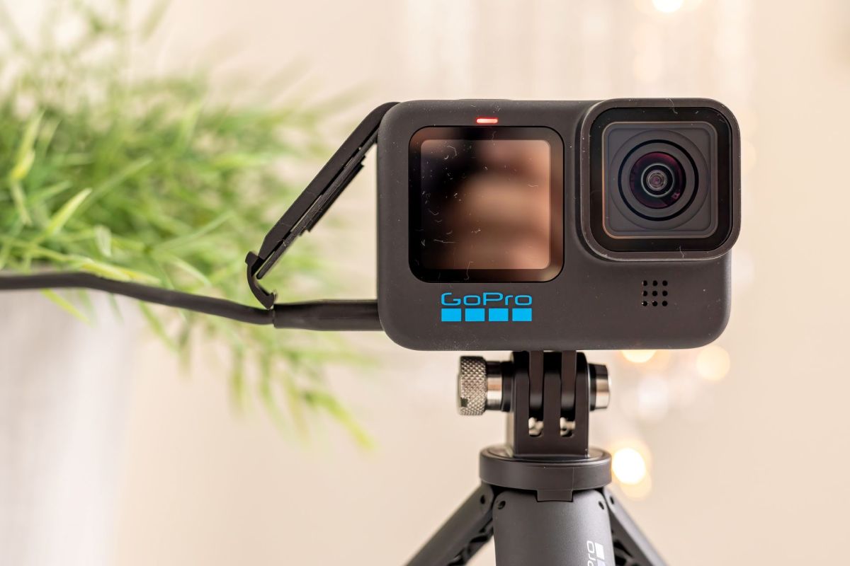 A GoPro camera mounted on a tripod with blurred greenery in the background.
