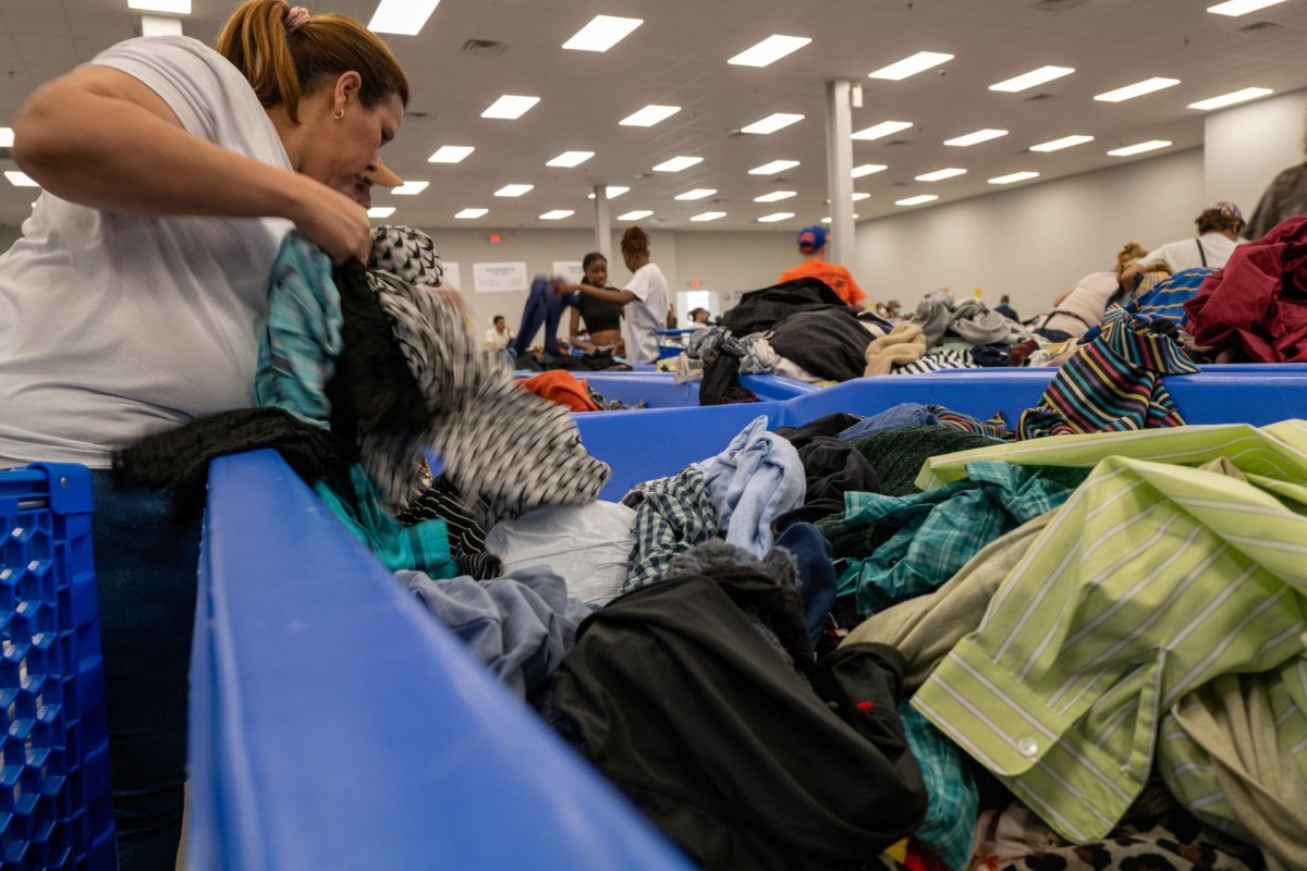 A woman sorts through piles of clothing in a large, open space filled with bins.
