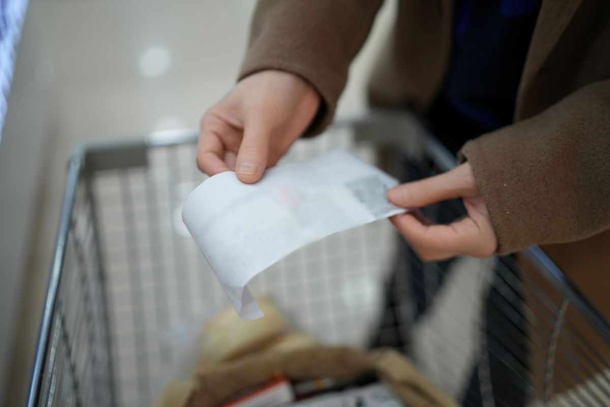 A person holds a receipt above a shopping cart with bags.