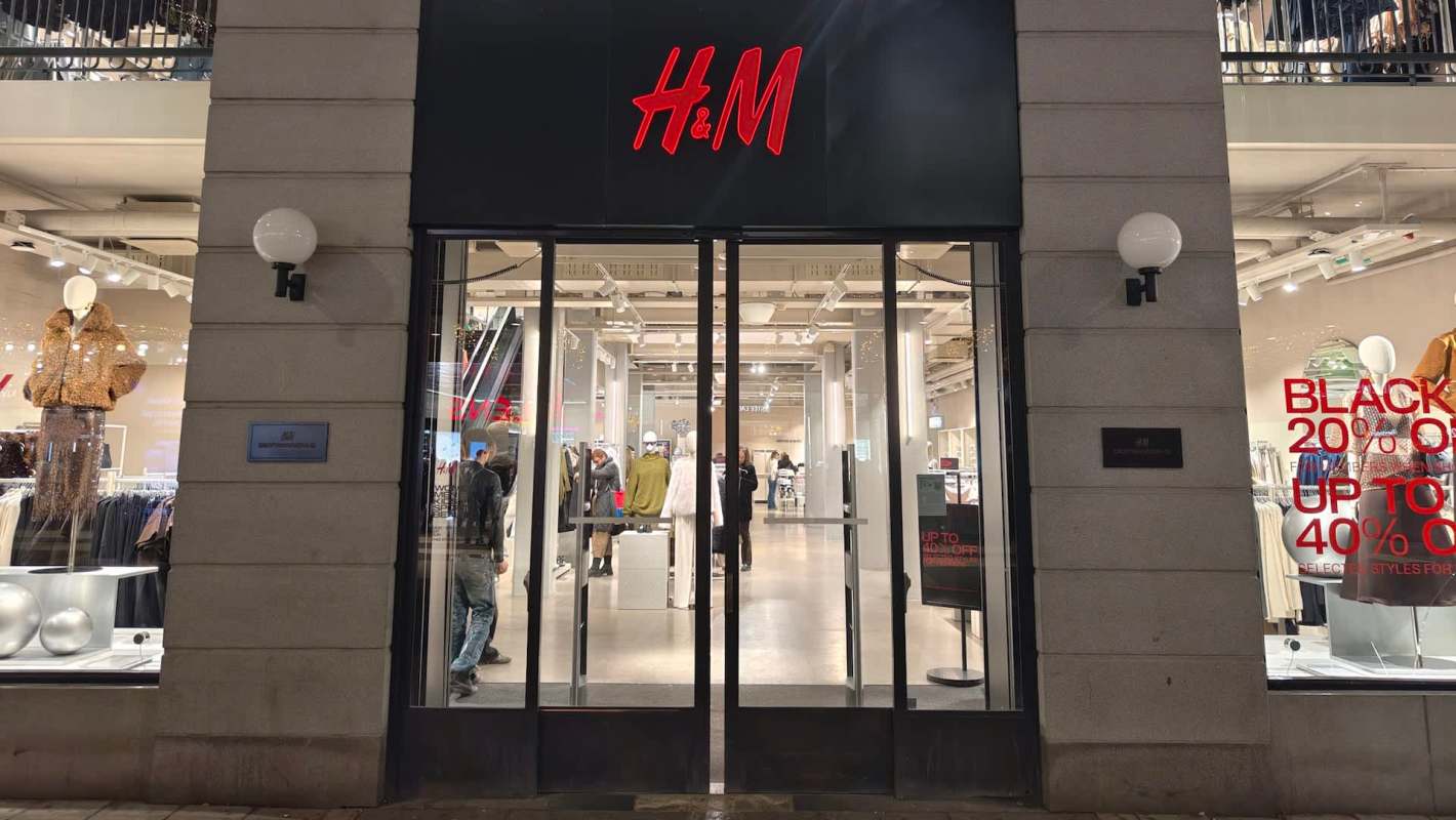 A night scene of the entrance of an H&M store showcasing clothing and promotional signs.