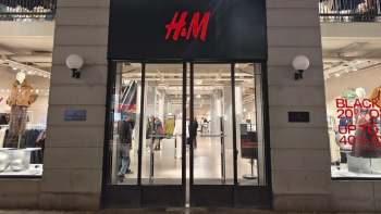 A night scene of the entrance of an H&M store showcasing clothing and promotional signs.