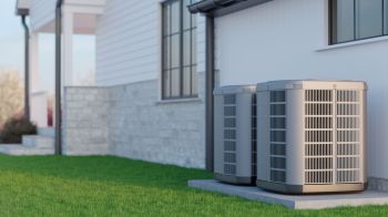 Two air conditioning units installed beside a house on a grassy area.