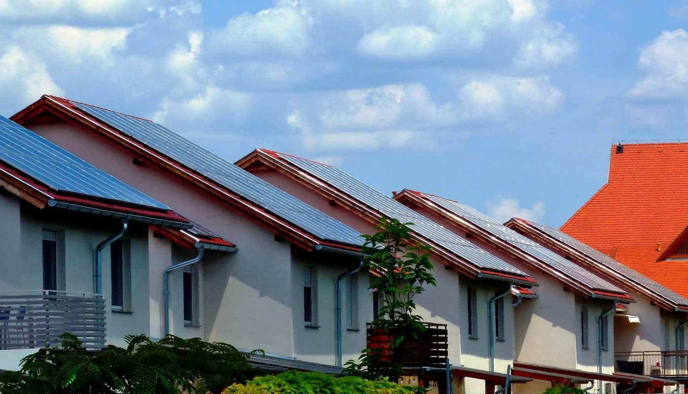 Houses with solar panels on the roofs under a cloudy sky.