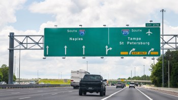 A highway sign indicating directions to Naples, Tampa, and St. Petersburg with vehicles on the road below.