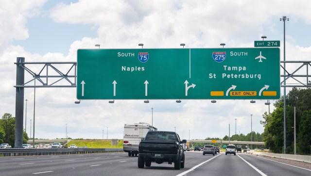 A highway sign indicating directions to Naples, Tampa, and St. Petersburg with vehicles on the road below.