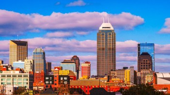 A Indianapolis skyline view of urban buildings against a blue sky with clouds.