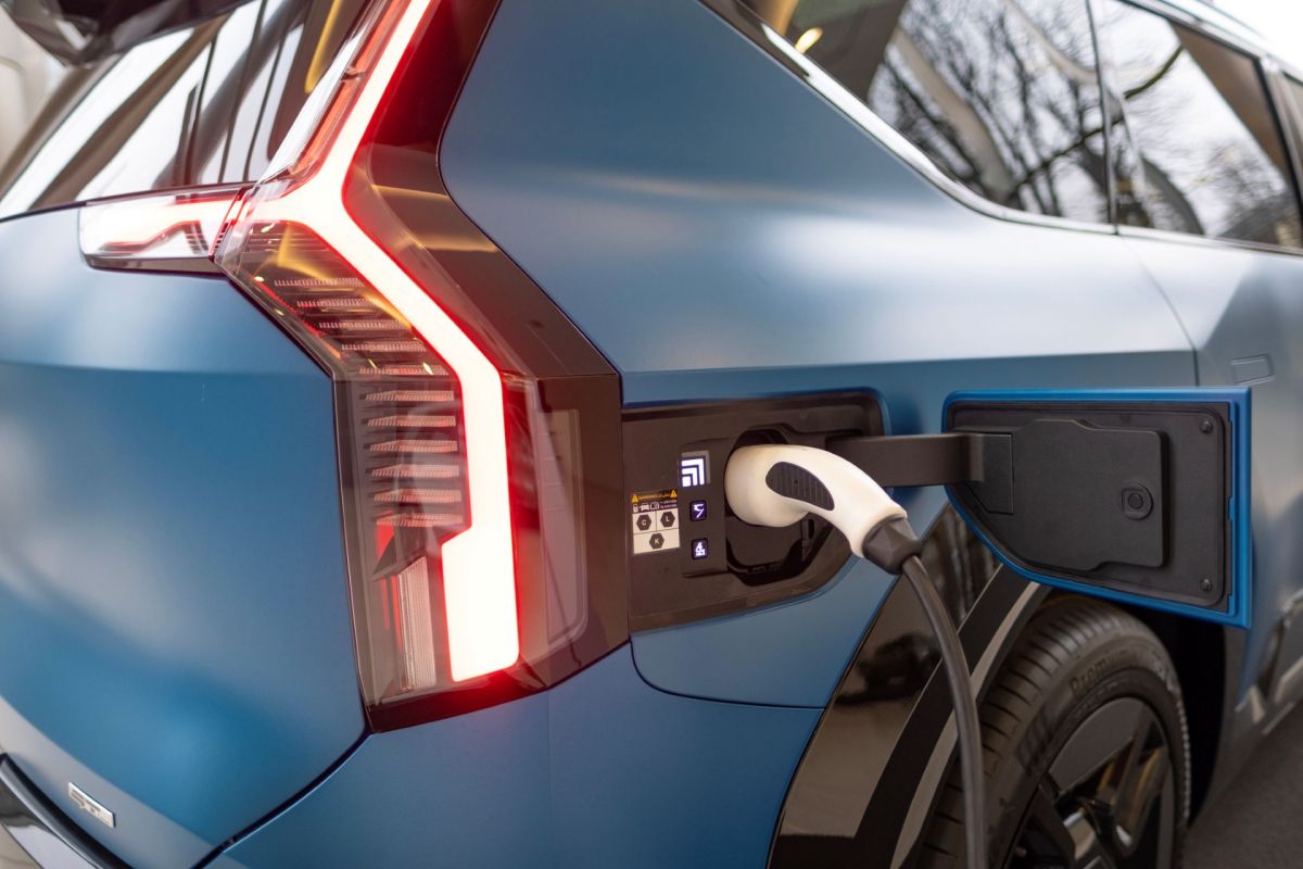 A Kia EV9 electric vehicle is connected to a charging station, showing the charging port and cable.