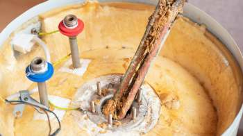 An exposed water heater tank with metal rods and deteriorating insulation material.