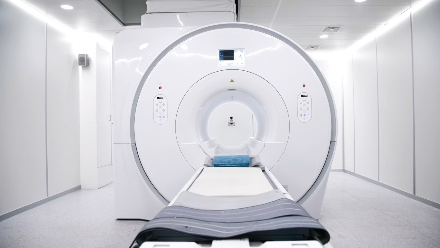 An MRI machine in a clinical room with white walls and a padded examination table.