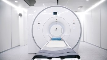 An MRI machine in a clinical room with white walls and a padded examination table.