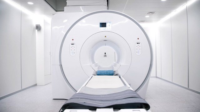 An MRI machine in a clinical room with white walls and a padded examination table.