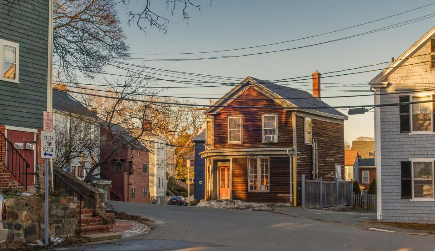A street scene featuring a vintage house, utility wires, and a street sign with directions to Salem and Boston.