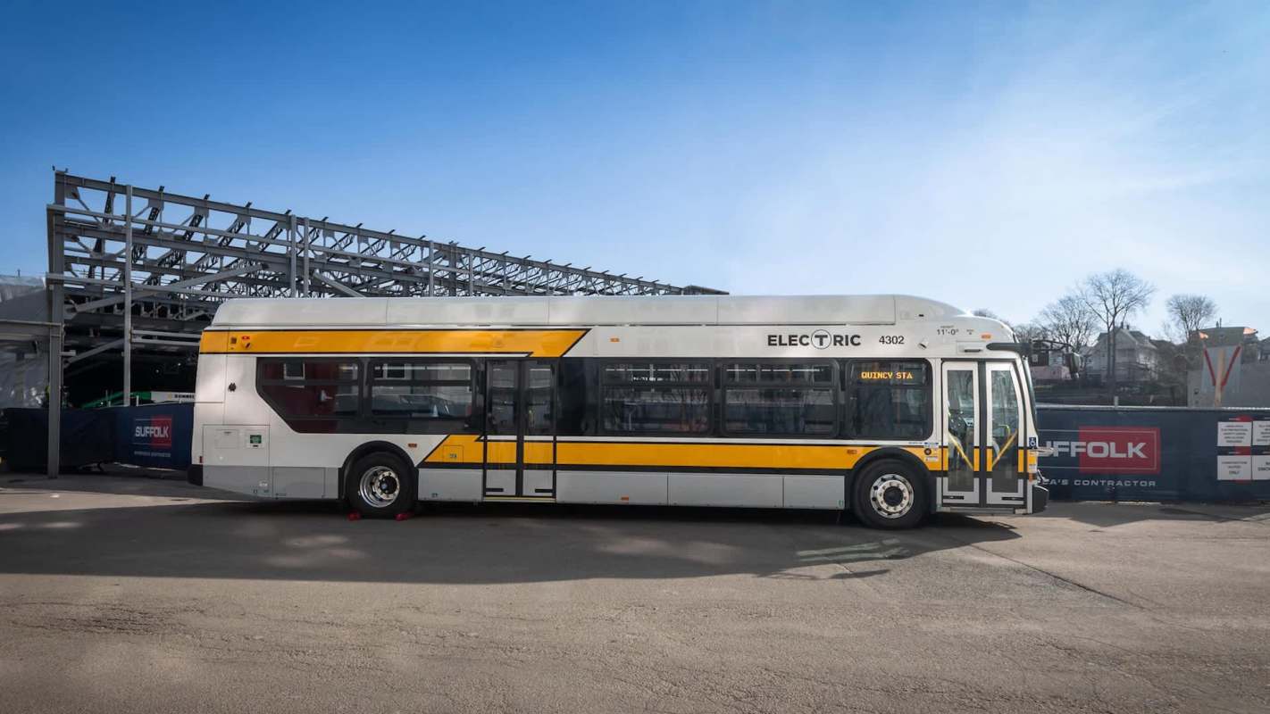 An electric bus parked near a construction site with a partially built structure in the background.