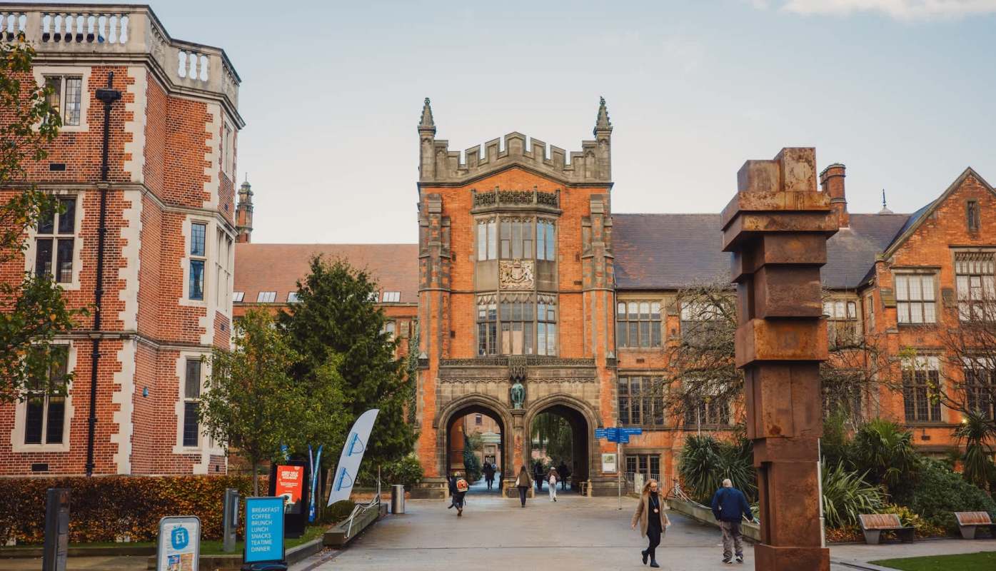 A university building with brick architecture, an archway, and a modern sculpture in the foreground.