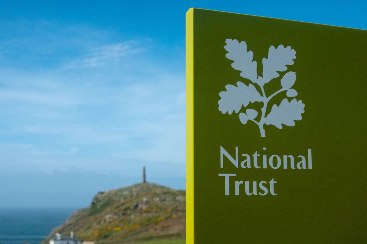 A National Trust sign with an oak leaf and a coastal landscape in the background.
