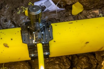A yellow natural gas pipeline with a black attachment in muddy surroundings.