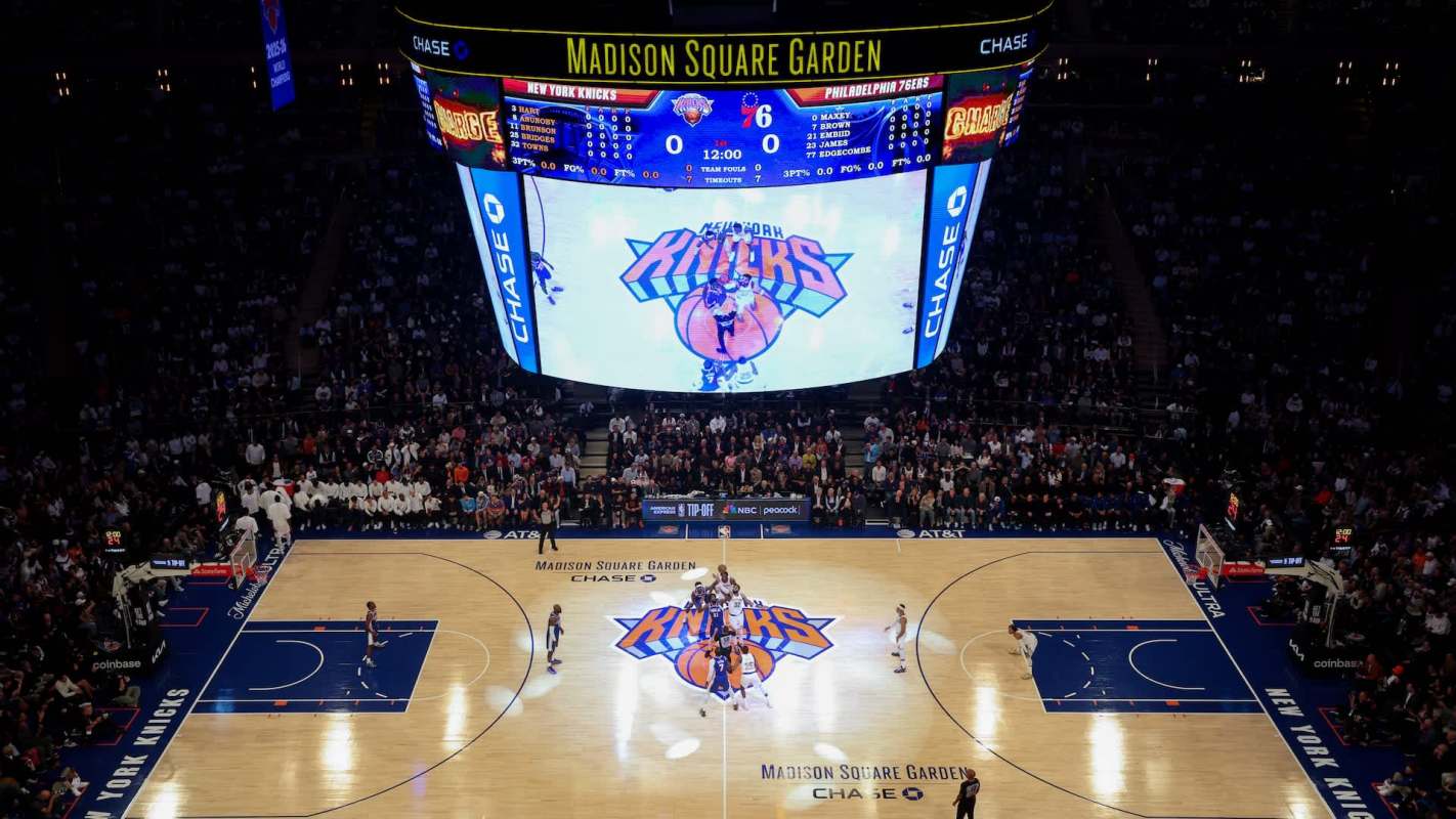 A basketball game underway at Madison Square Garden with fans in the stands and a large scoreboard overhead.