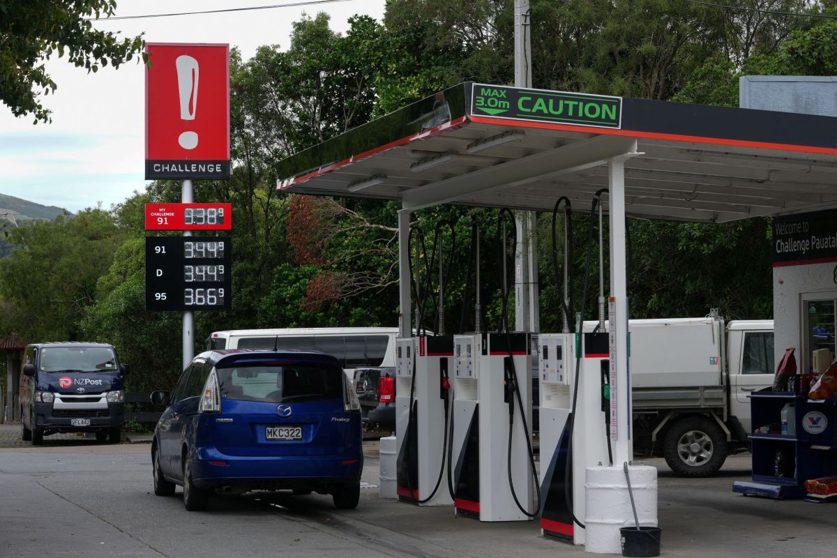A gas station in New Zealand with a price sign displaying fuel prices and a blue car parked nearby.