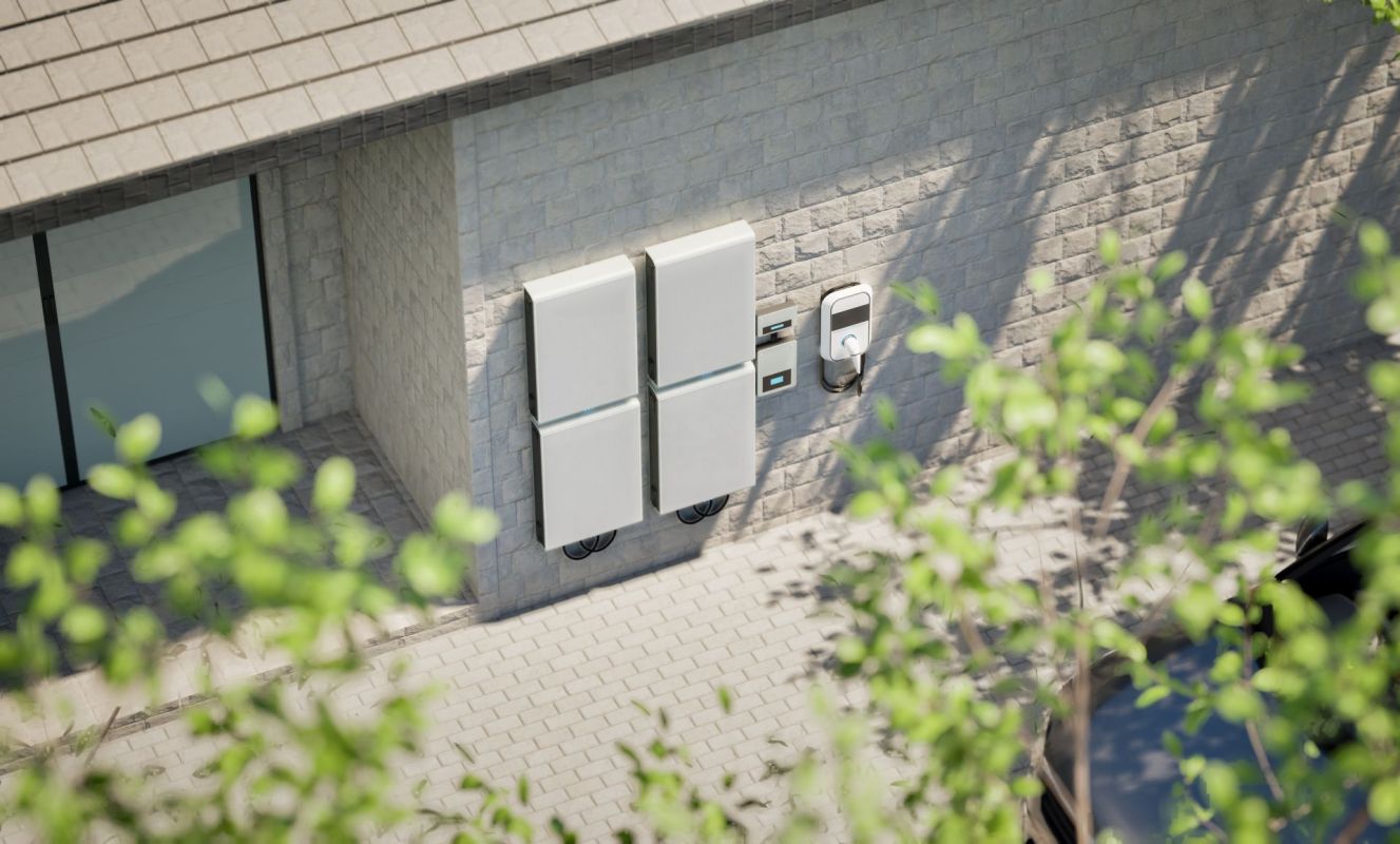 Two energy storage units and a charging station are mounted on a stone wall next to a paved area.