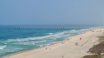 A beach scene with a pier, waves, and several people walking along the sand.