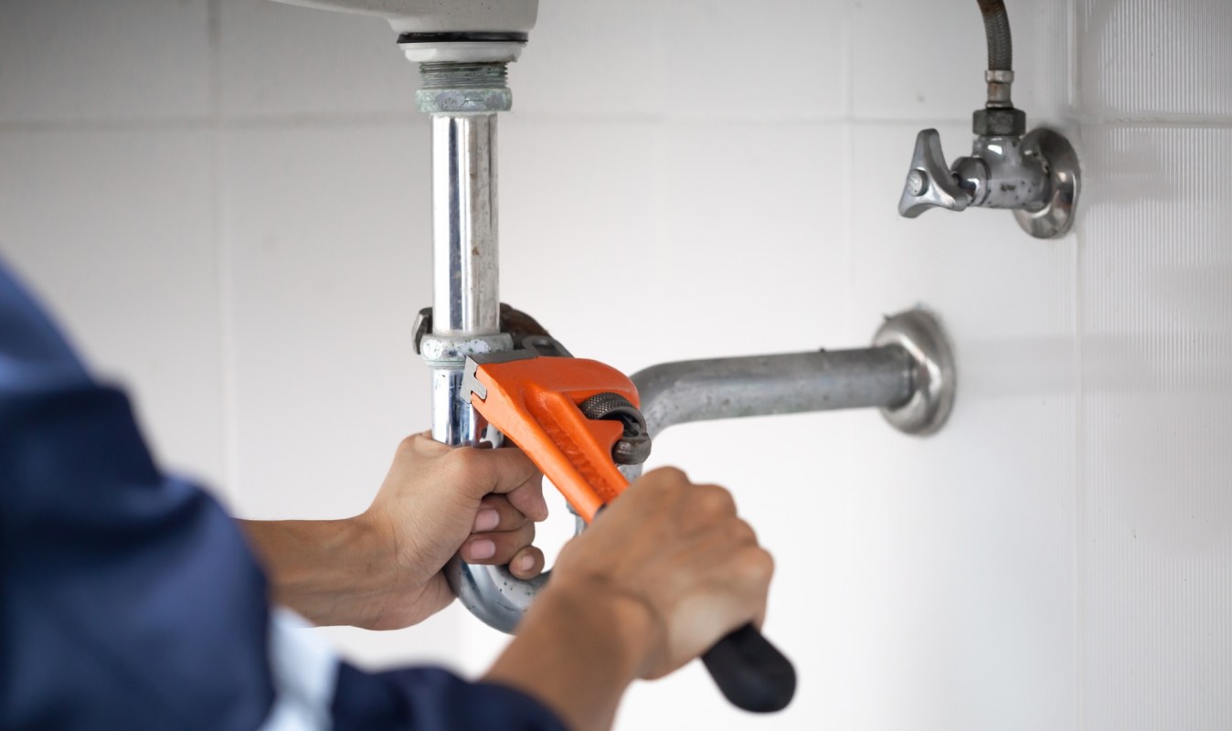A person uses a wrench to tighten a plumbing pipe connection.