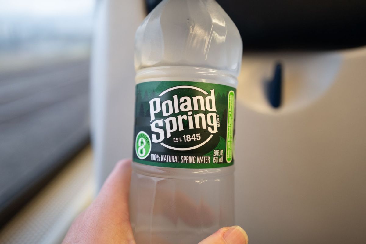 A hand holding a bottle of Poland Spring water inside a train.