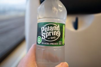 A hand holding a bottle of Poland Spring water inside a train.