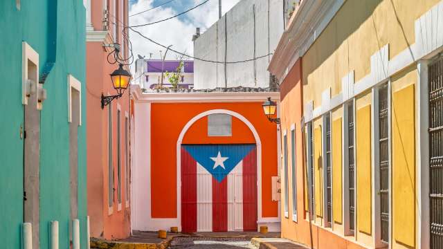 A door painted with a Puerto Rican flag on a street with brightly colored buildings.