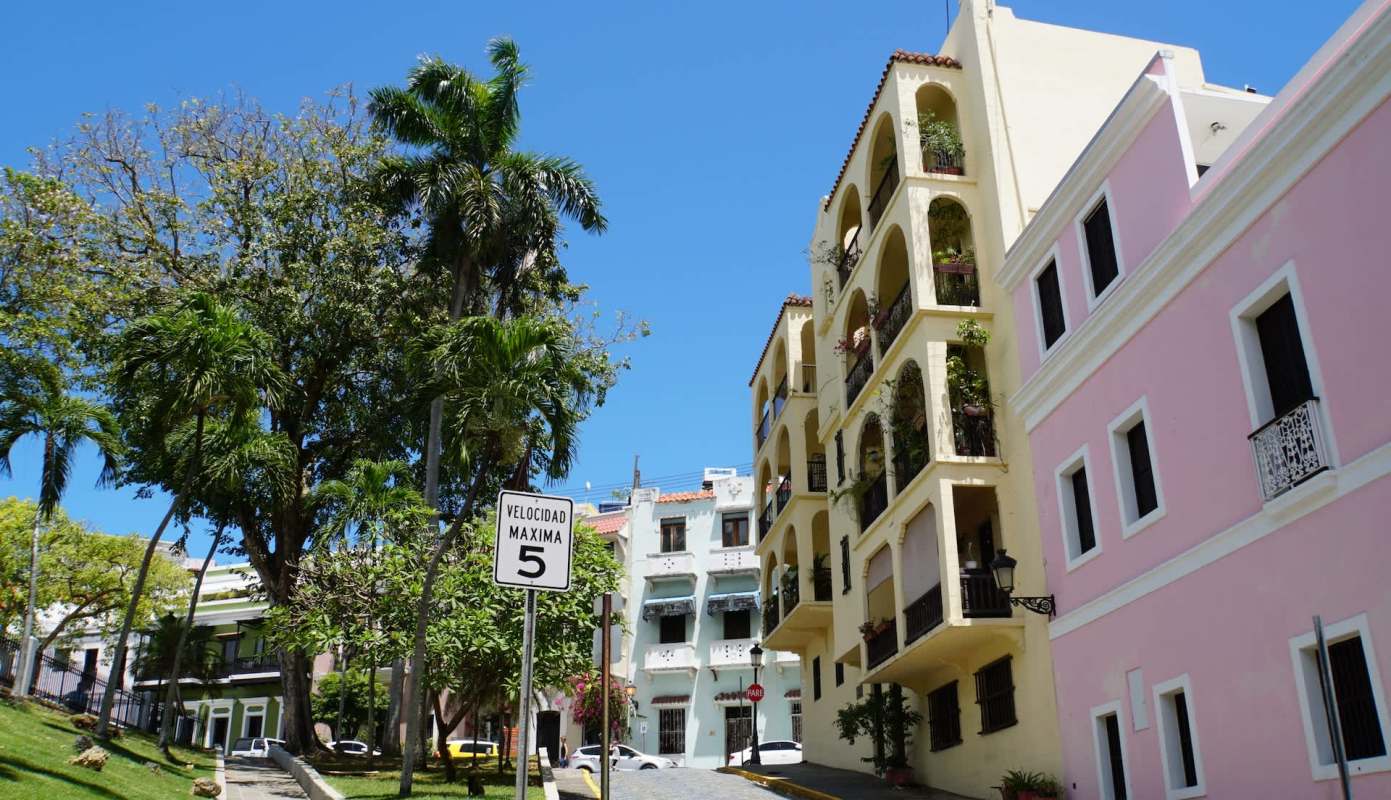 A street view featuring colorful buildings, palm trees, and a speed limit sign.