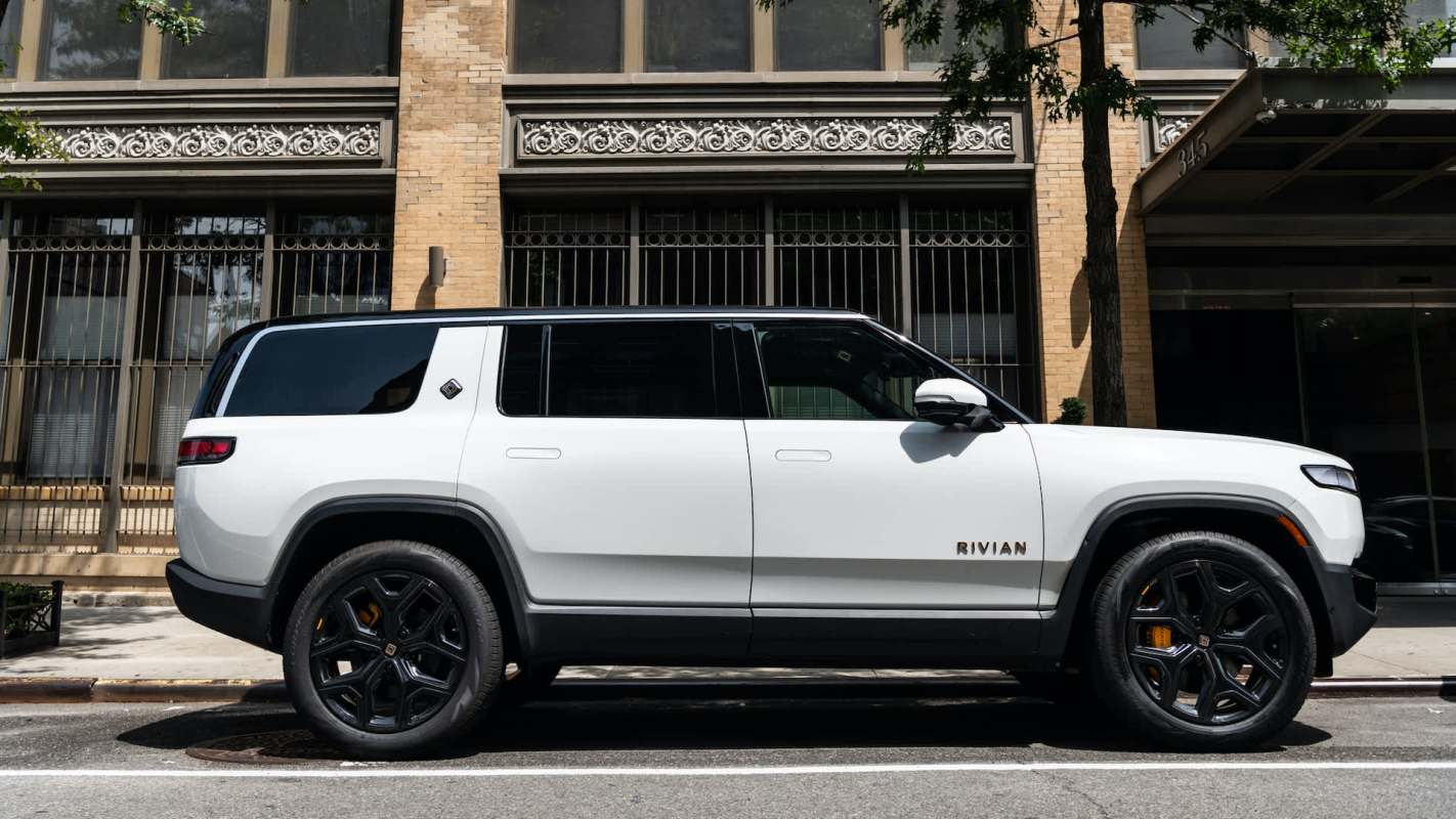 A white electric SUV parked on the street next to a brick building.