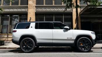 A white electric SUV parked on the street next to a brick building.
